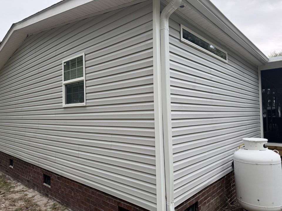 Gray vinyl siding on a house with a small window, gutter, and propane tank.