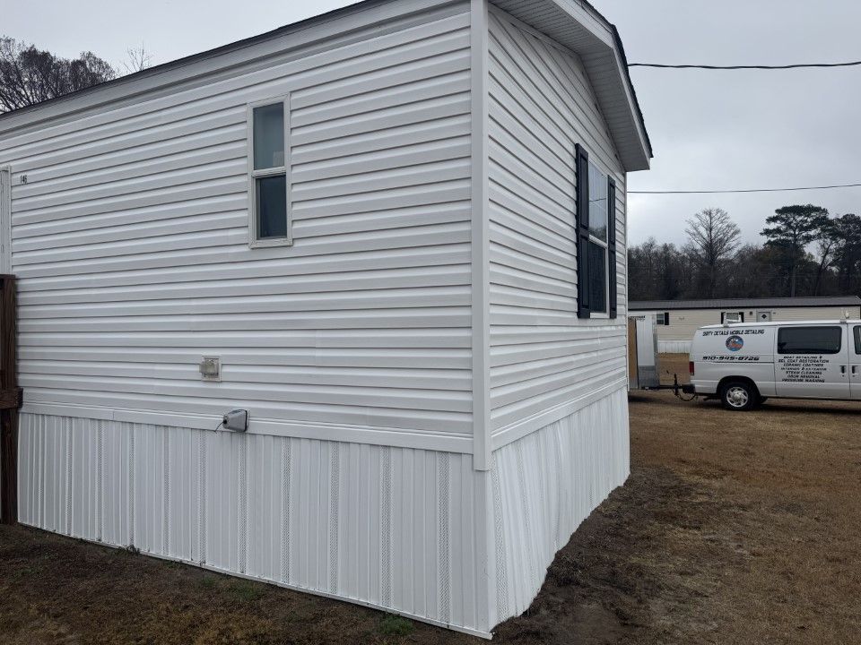 White vinyl-sided mobile home with a small window and a black shutter on the corner, outdoors.