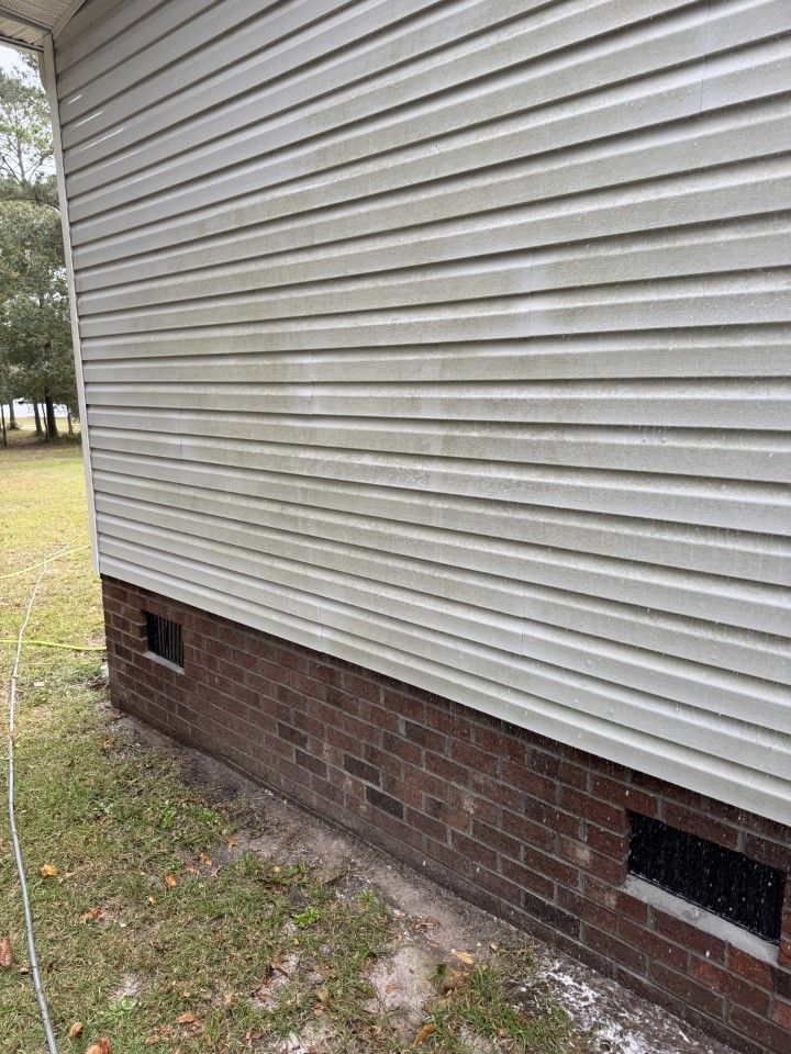 Light-colored siding on a house with a brick foundation, a lawn in front, and a dark vent.