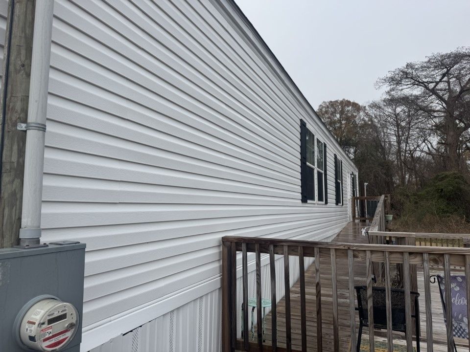 White vinyl siding on a building with a deck and electrical box, against a cloudy sky.