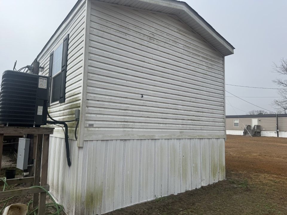 Side of a mobile home with faded white siding, air conditioner unit, and weathered skirting.
