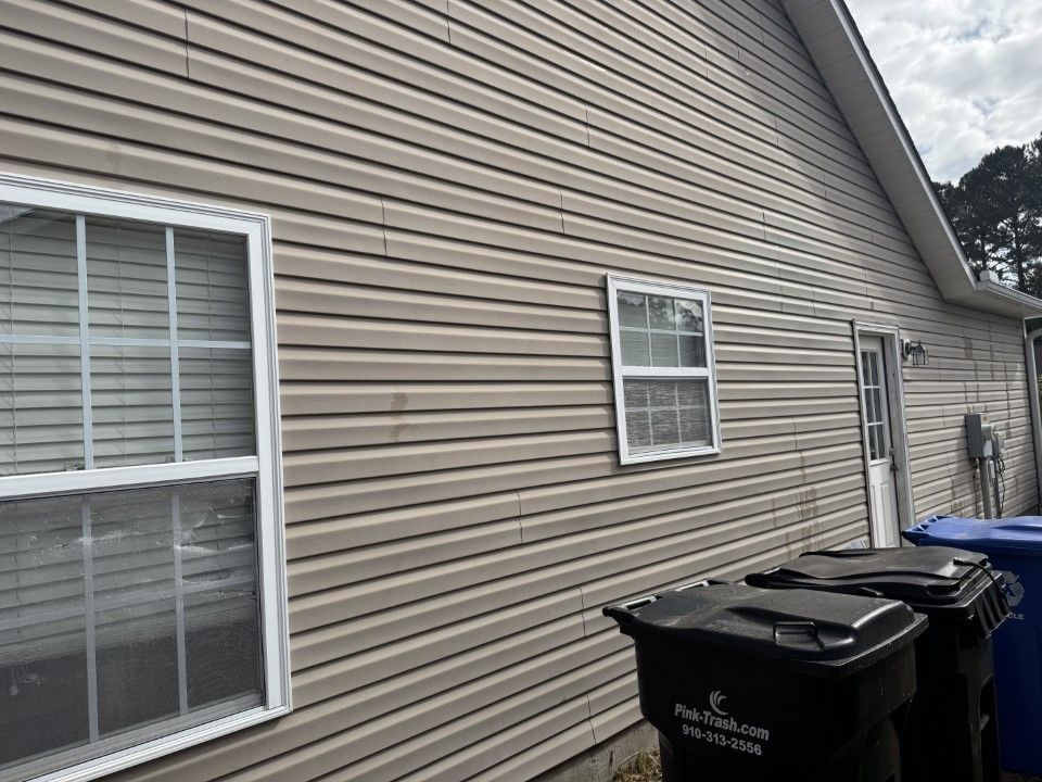Beige vinyl siding with white-framed windows and trash bins against the house.