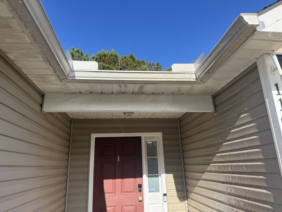 View of a home's covered entryway: red door, beige siding, white trim, gutters, blue sky.