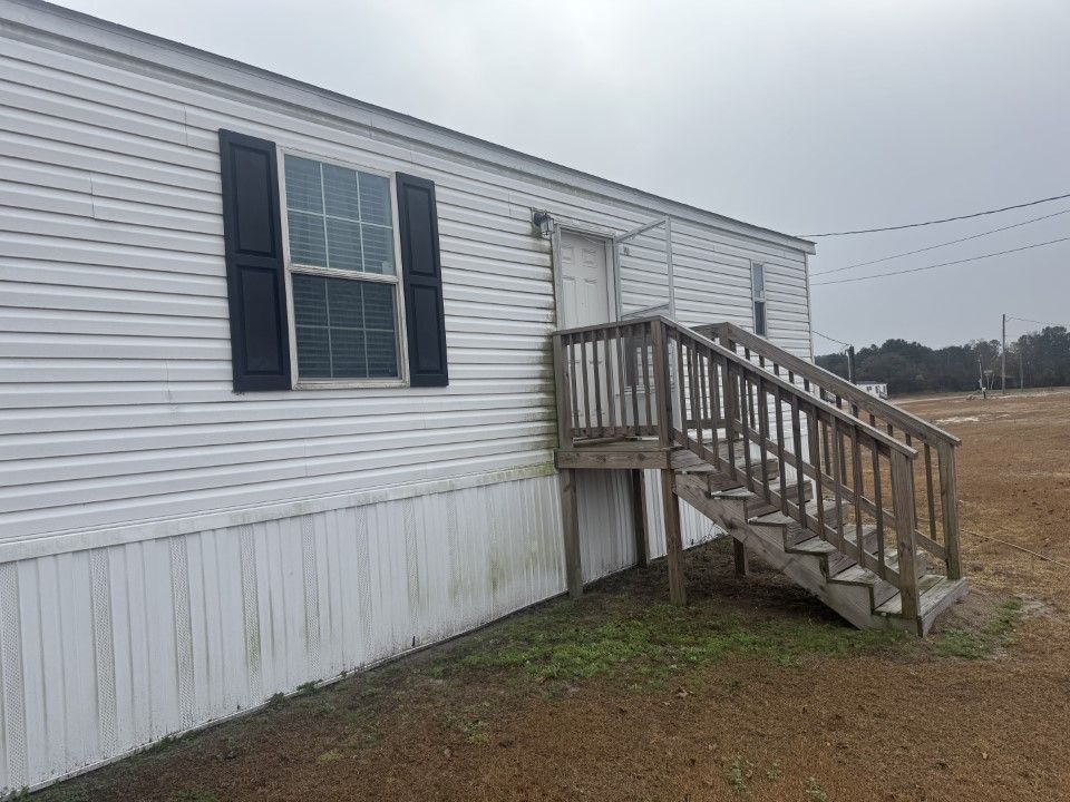 White mobile home with wooden stairs and dark shutters. Cloudy day.