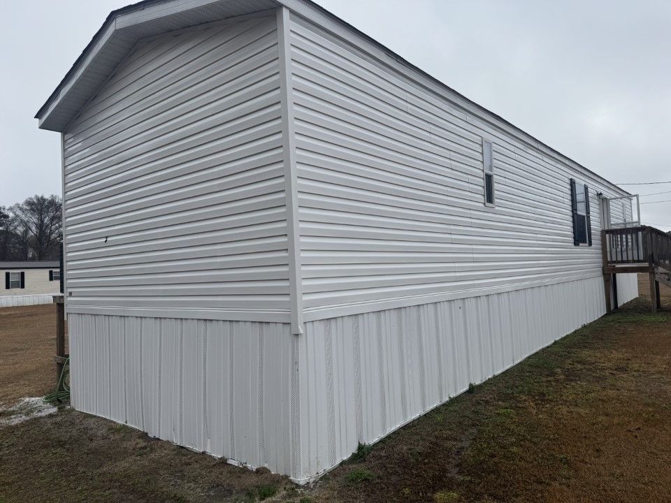 White mobile home with vinyl siding, set on a slight incline, on a cloudy day.