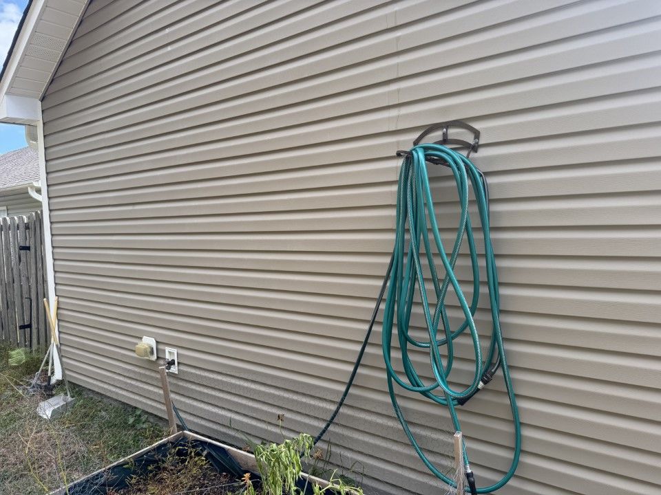 Beige vinyl siding with a green garden hose hanging on a dark metal bracket.