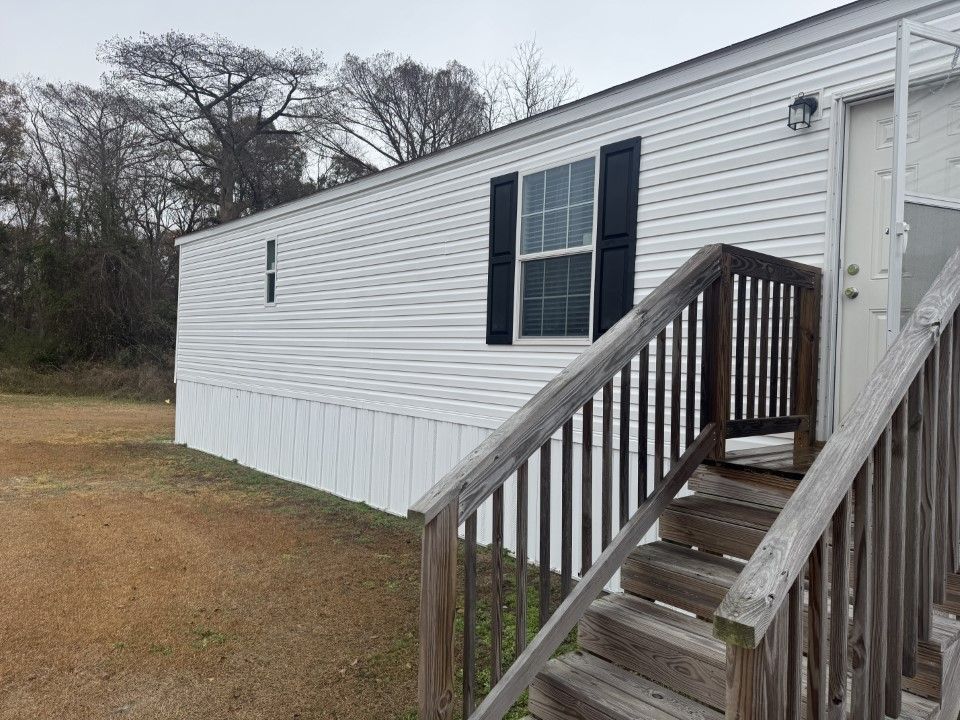 White mobile home with wooden stairs and black shutters.