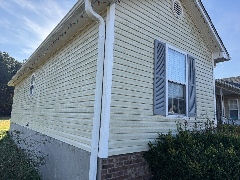 Beige vinyl-sided house with white trim, gray shutters, and a brick foundation.