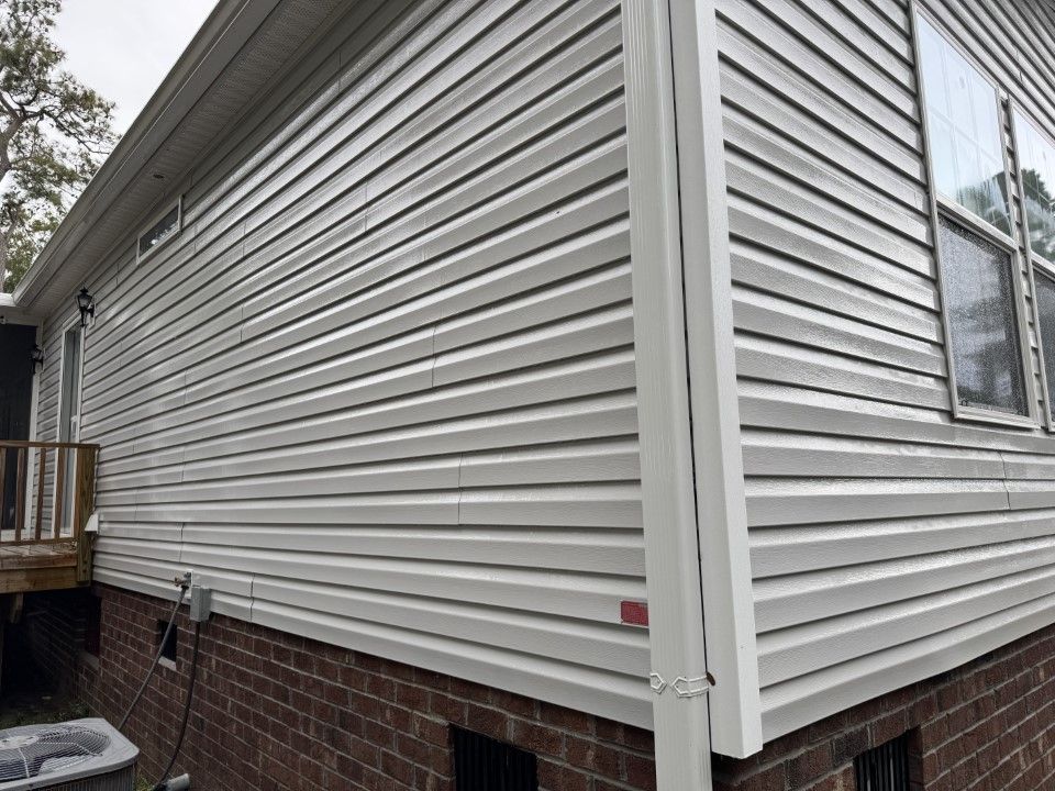 White vinyl siding on a house corner. Red brick foundation. White gutter and windows are visible.