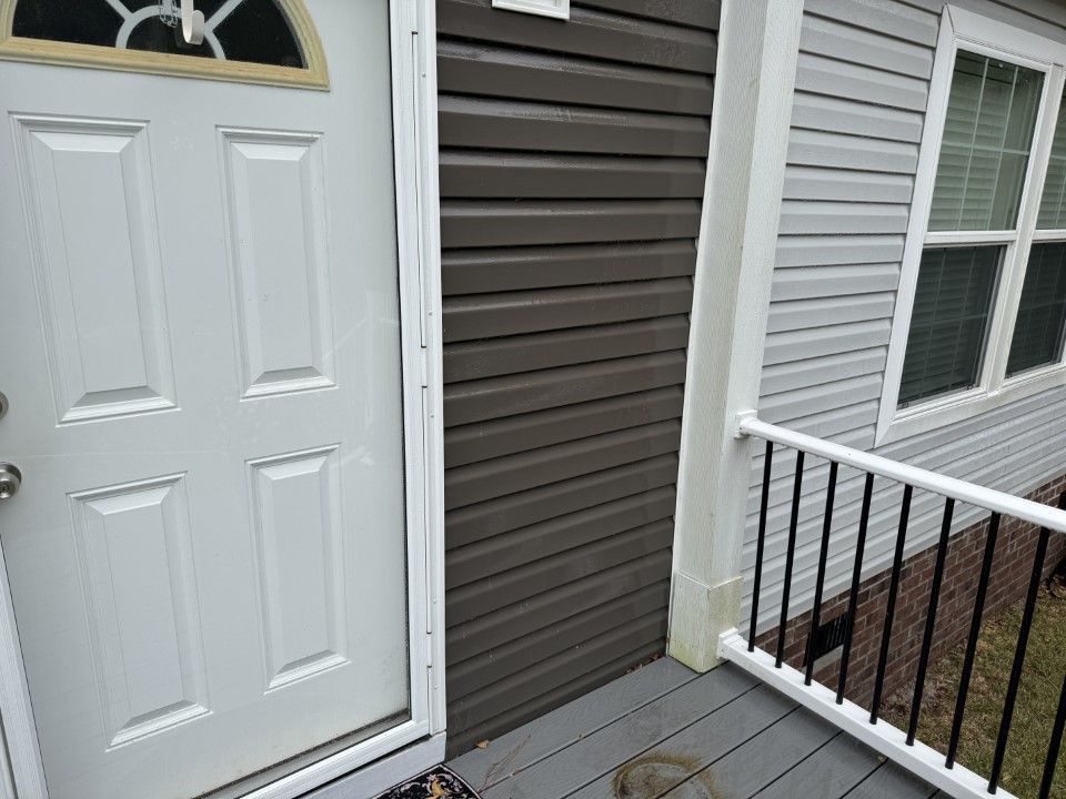 White front door next to gray siding, porch with railing.