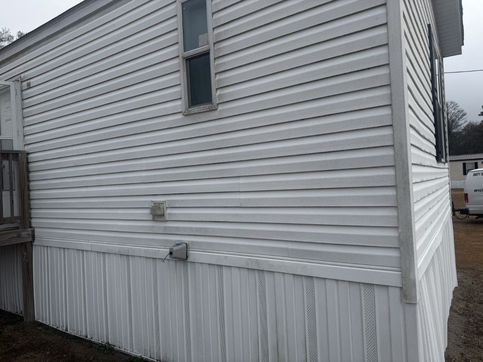 White vinyl-sided mobile home with horizontal siding above and vertical skirting below, a window, and two vents.