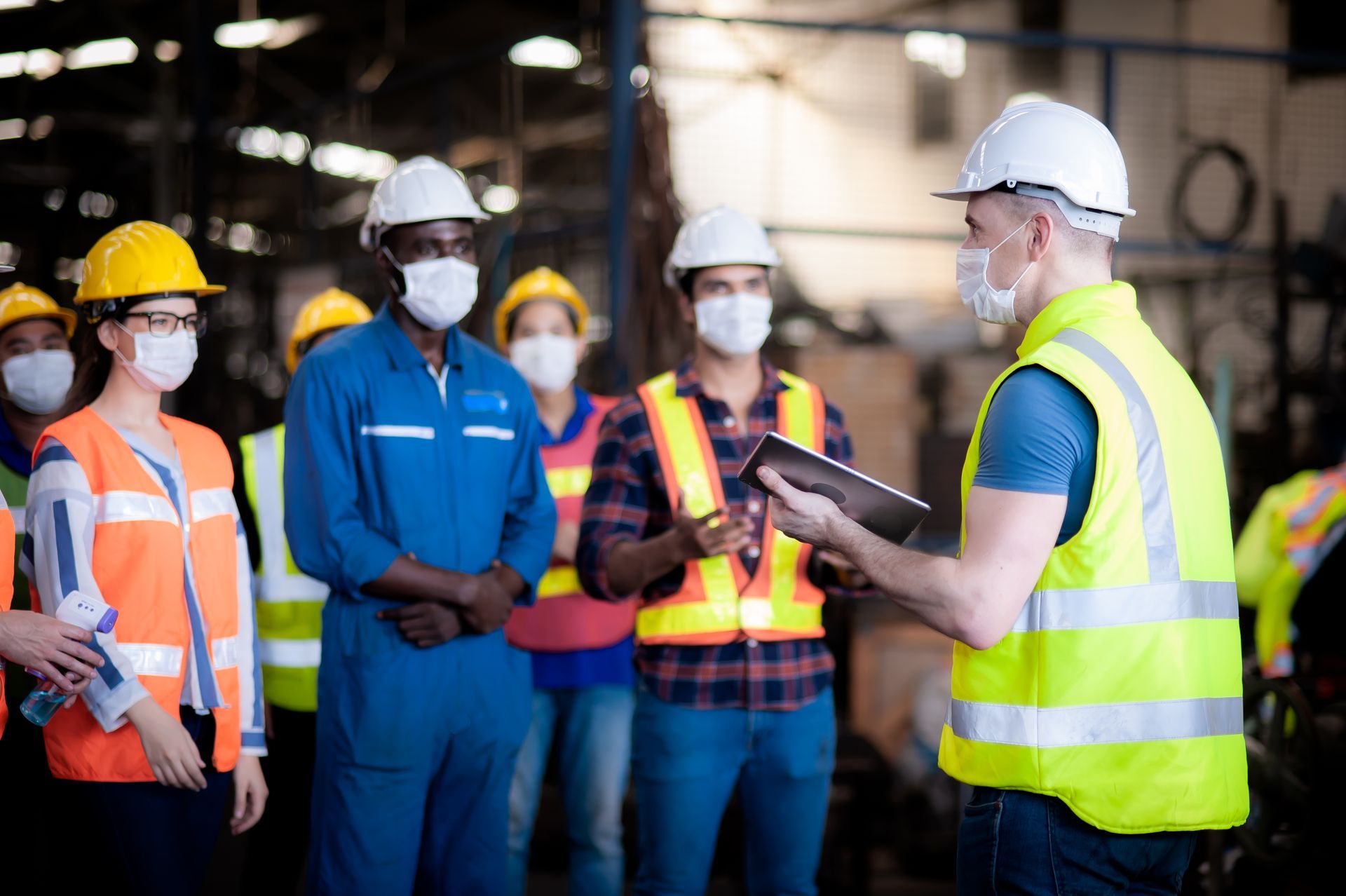 Construction workers in hard hats and safety vests listening to a supervisor on a job site.