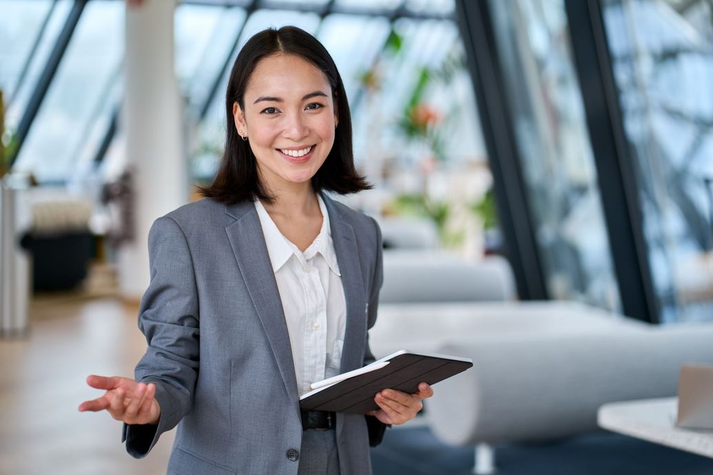 Smiling professional in gray blazer holding a tablet in a modern office lobby