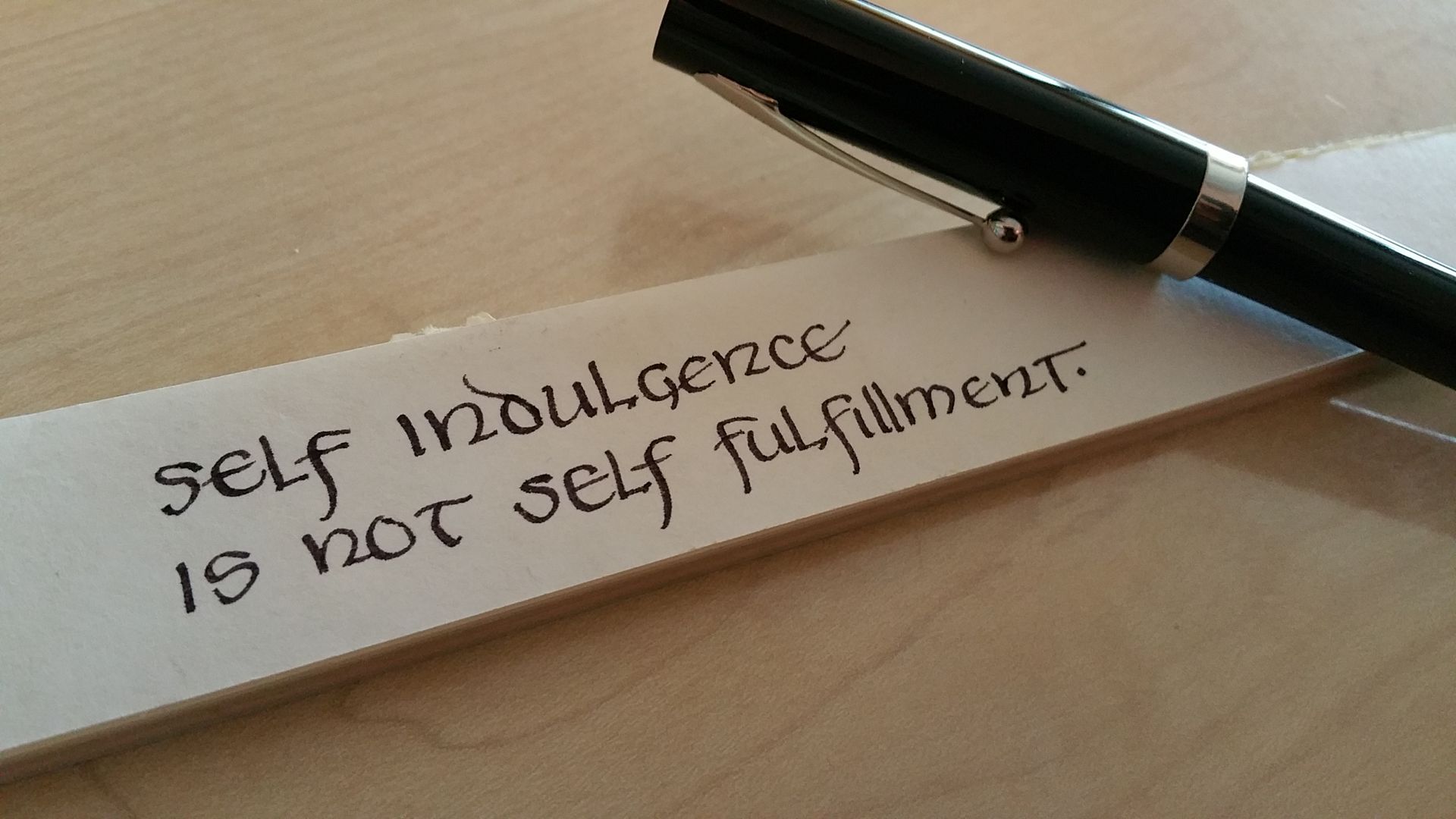 A pen rests on a piece of paper that says self indulgence is not self fulfillment