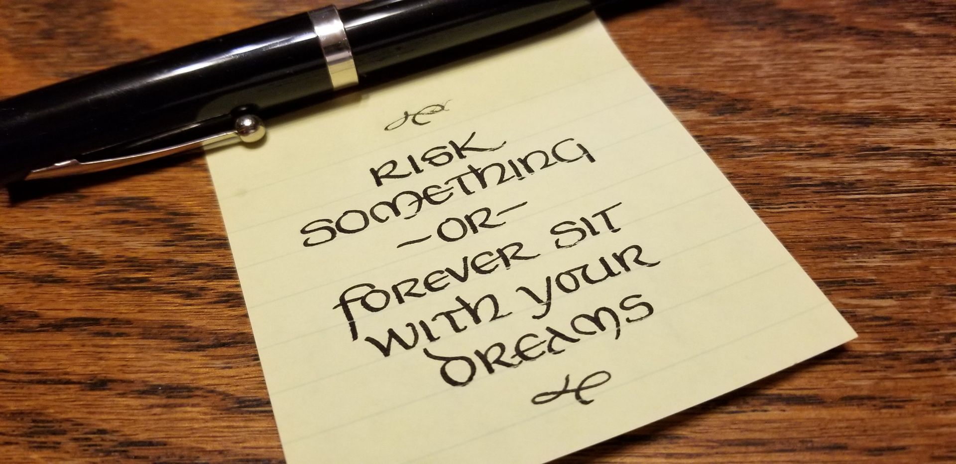 A note on a piece of paper that says risk something or forever sit with your dreams