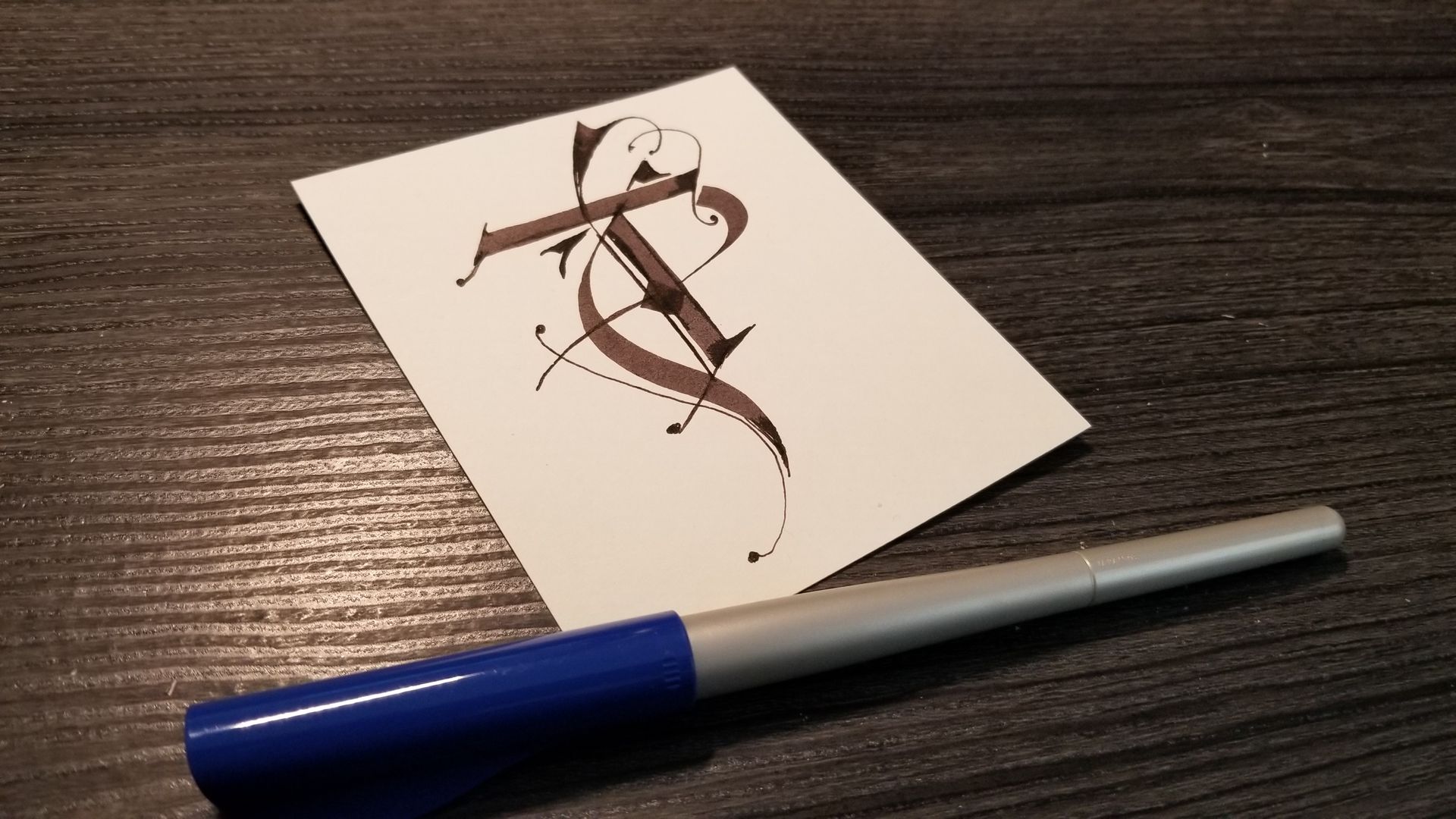 A pen is sitting next to a piece of paper with the letter t on it