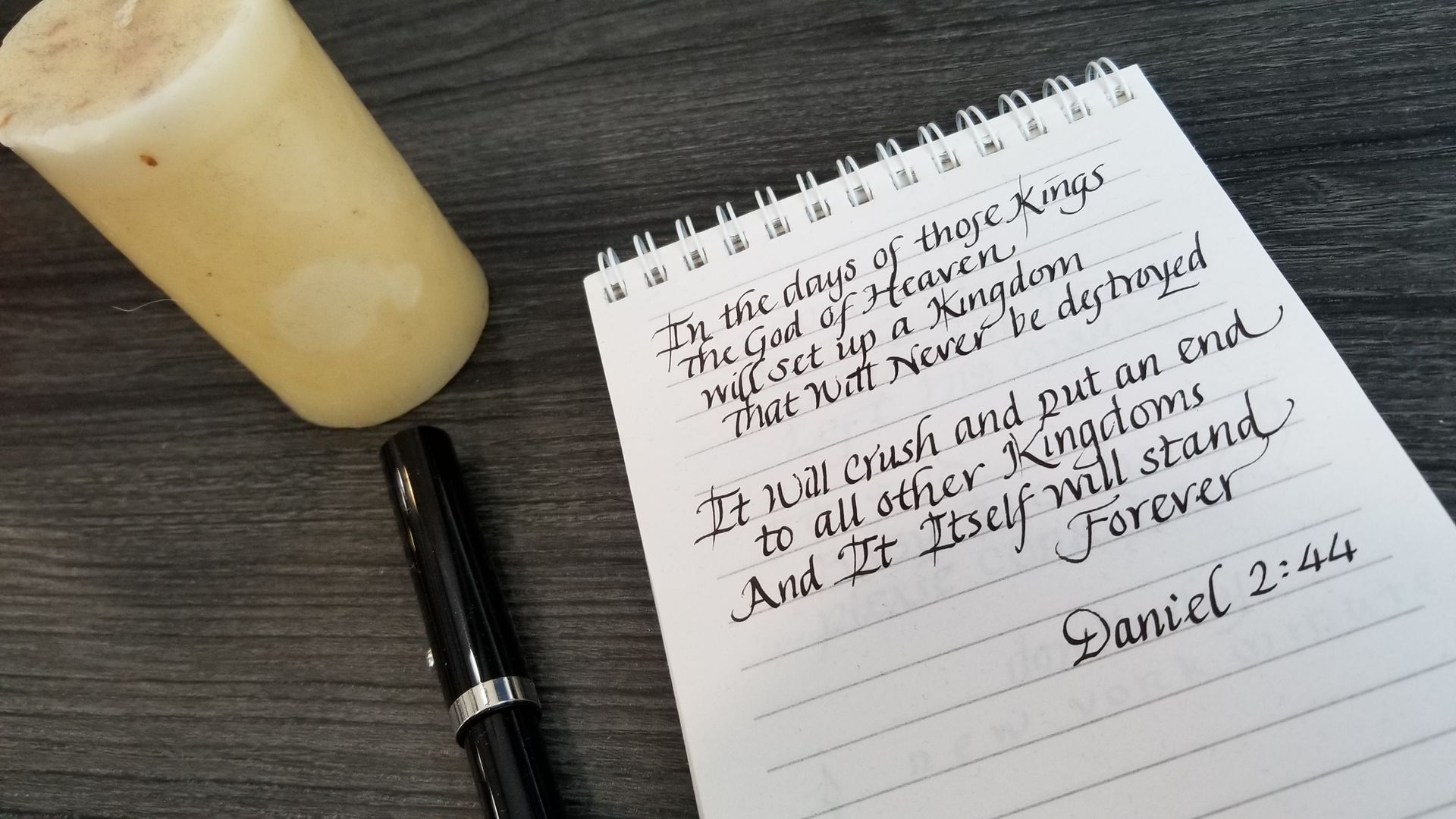A notebook with daniel 2 44 written on it next to a pen