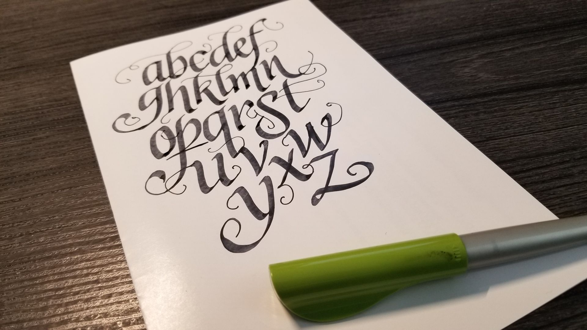 A pen is sitting on a piece of paper with the alphabet written on it.