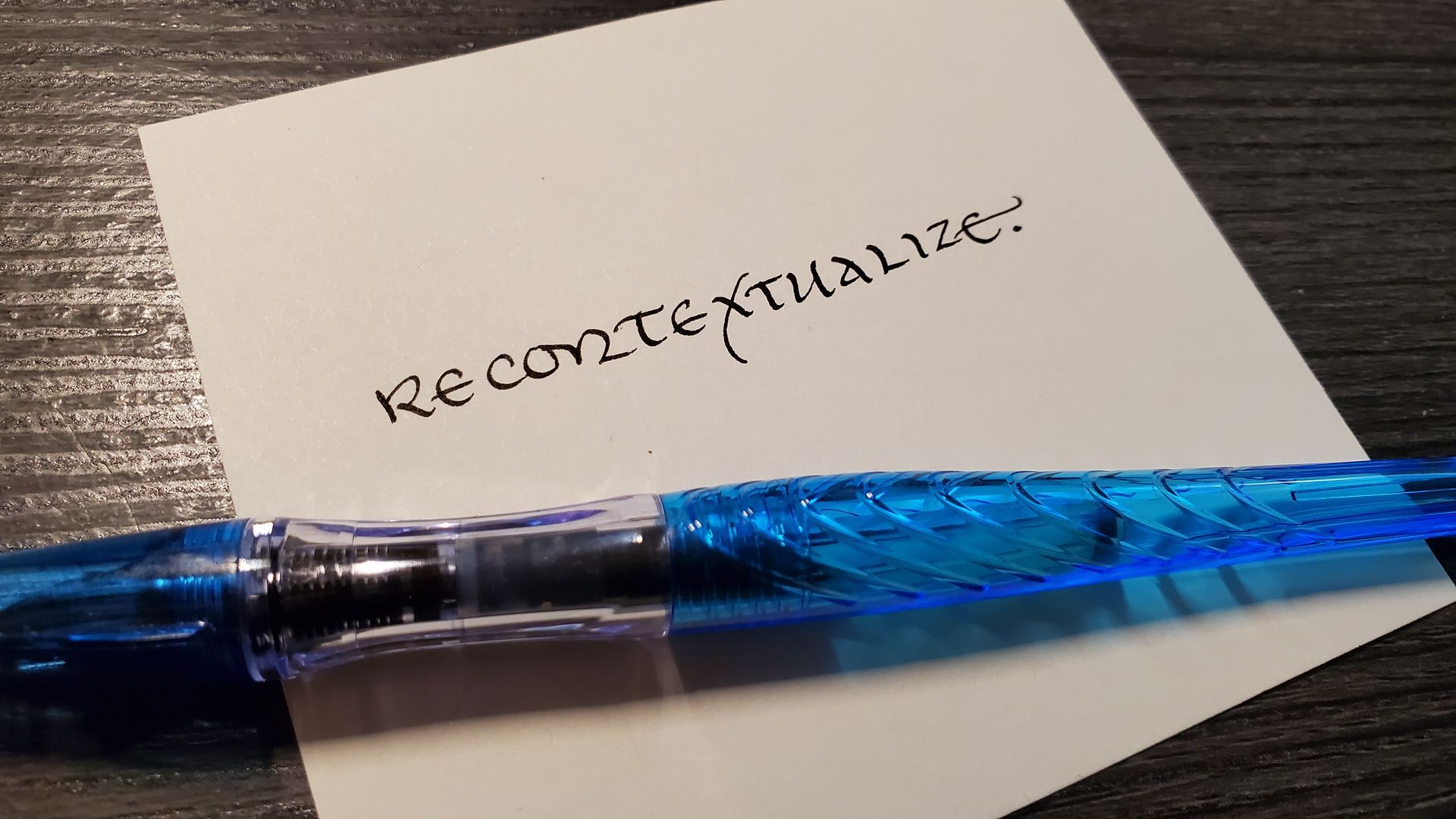 A blue pen is sitting on a piece of paper that says recontextualize