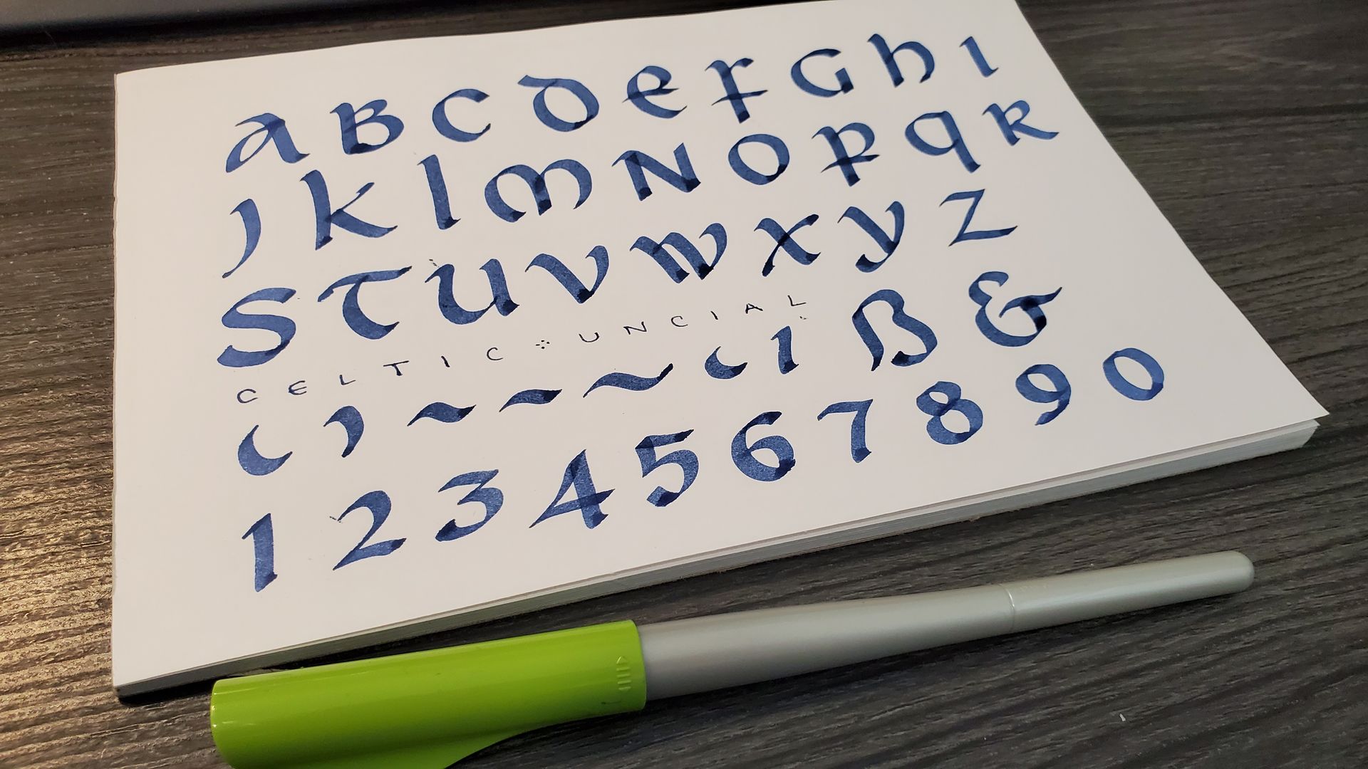 A piece of paper with the alphabet and numbers on it next to a pen