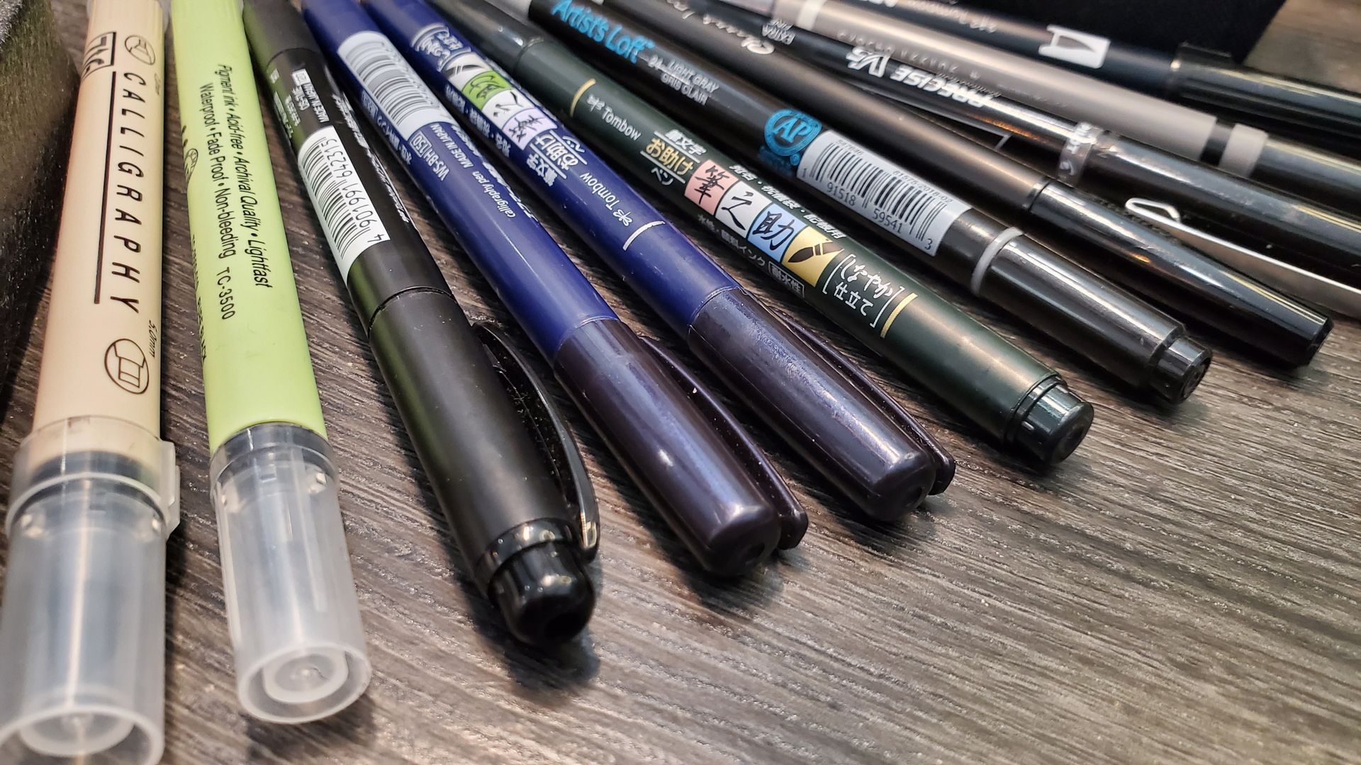 A bunch of pens are sitting on a wooden table.