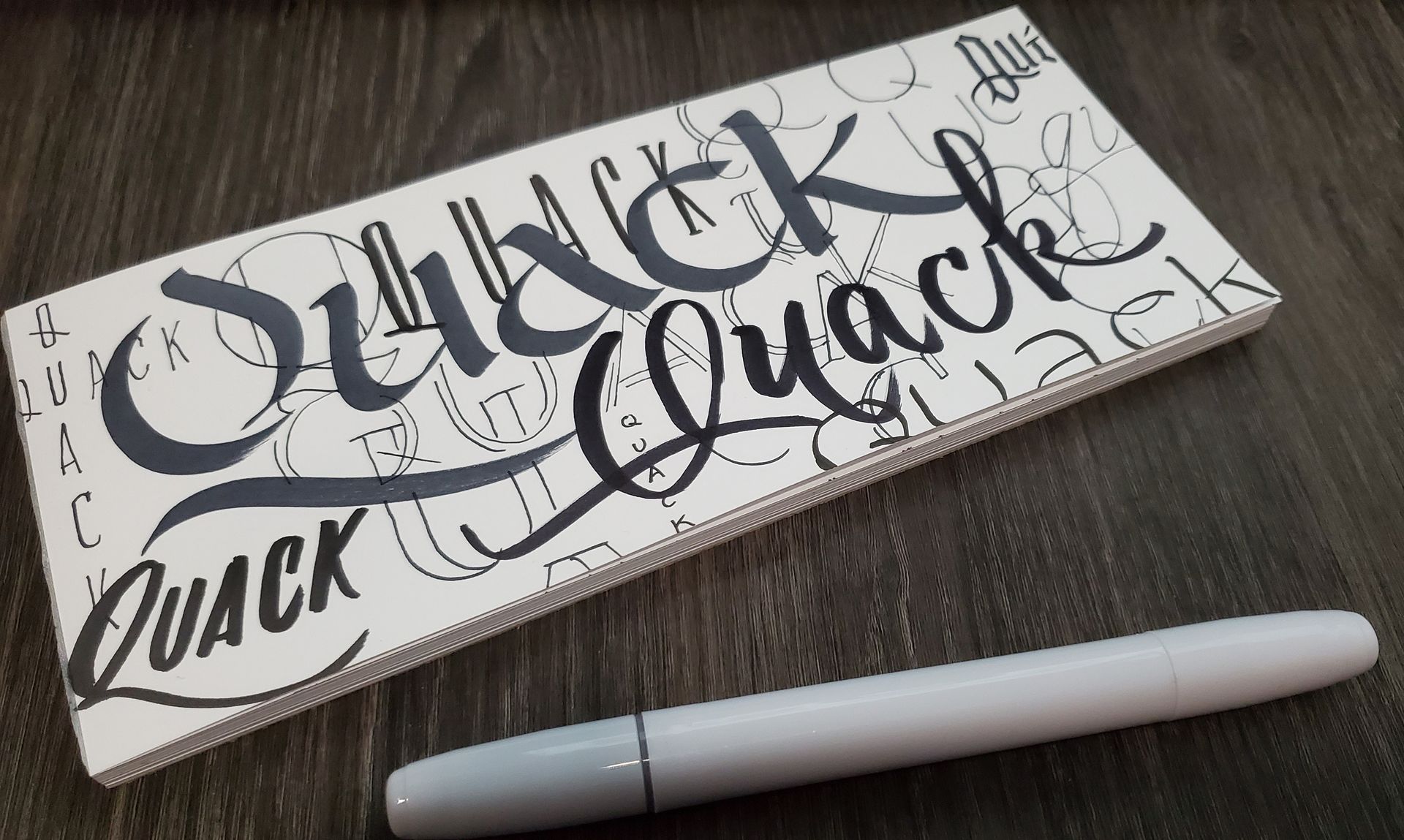 A notepad that says duck quack quack next to a pen