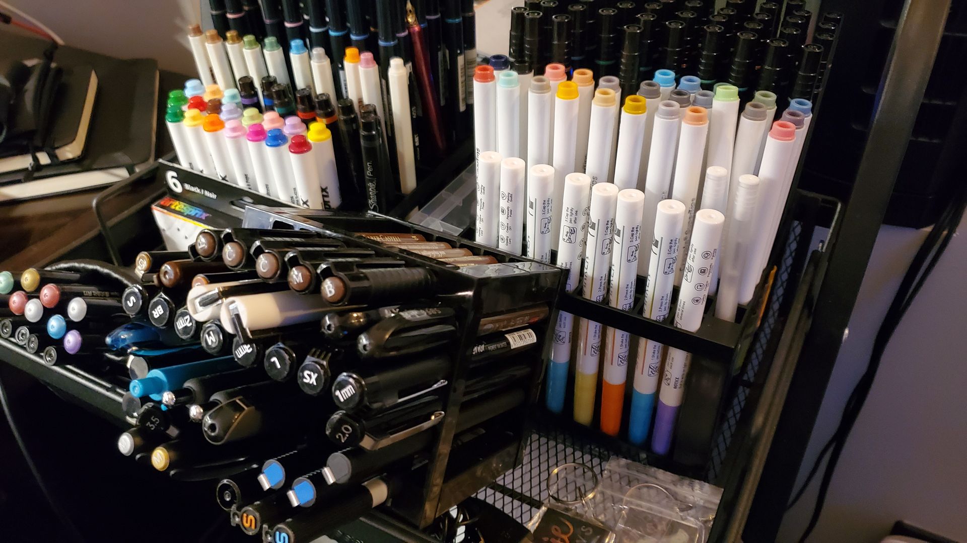 A bunch of pens and markers are stacked on top of each other on a table.