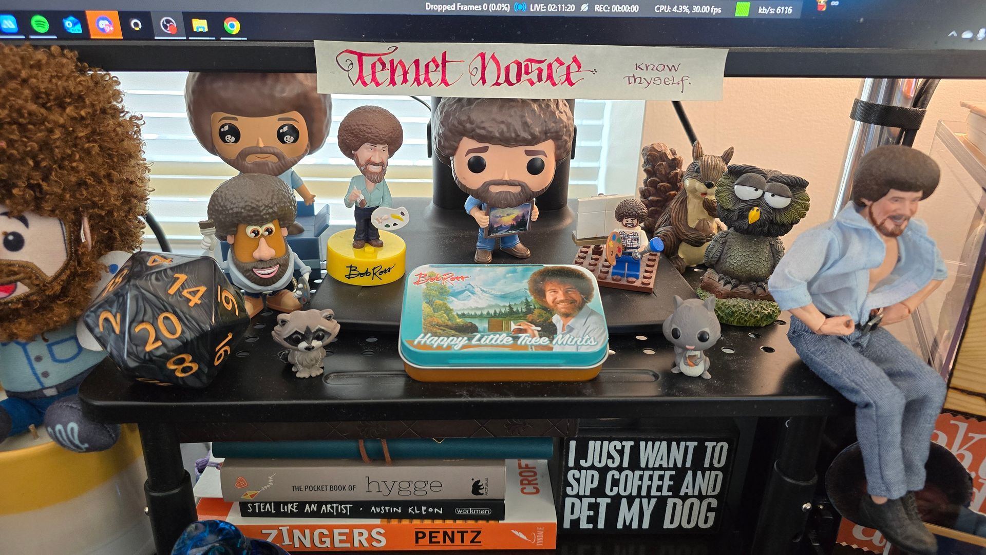 A shelf filled with lots of bob ross toys and books.