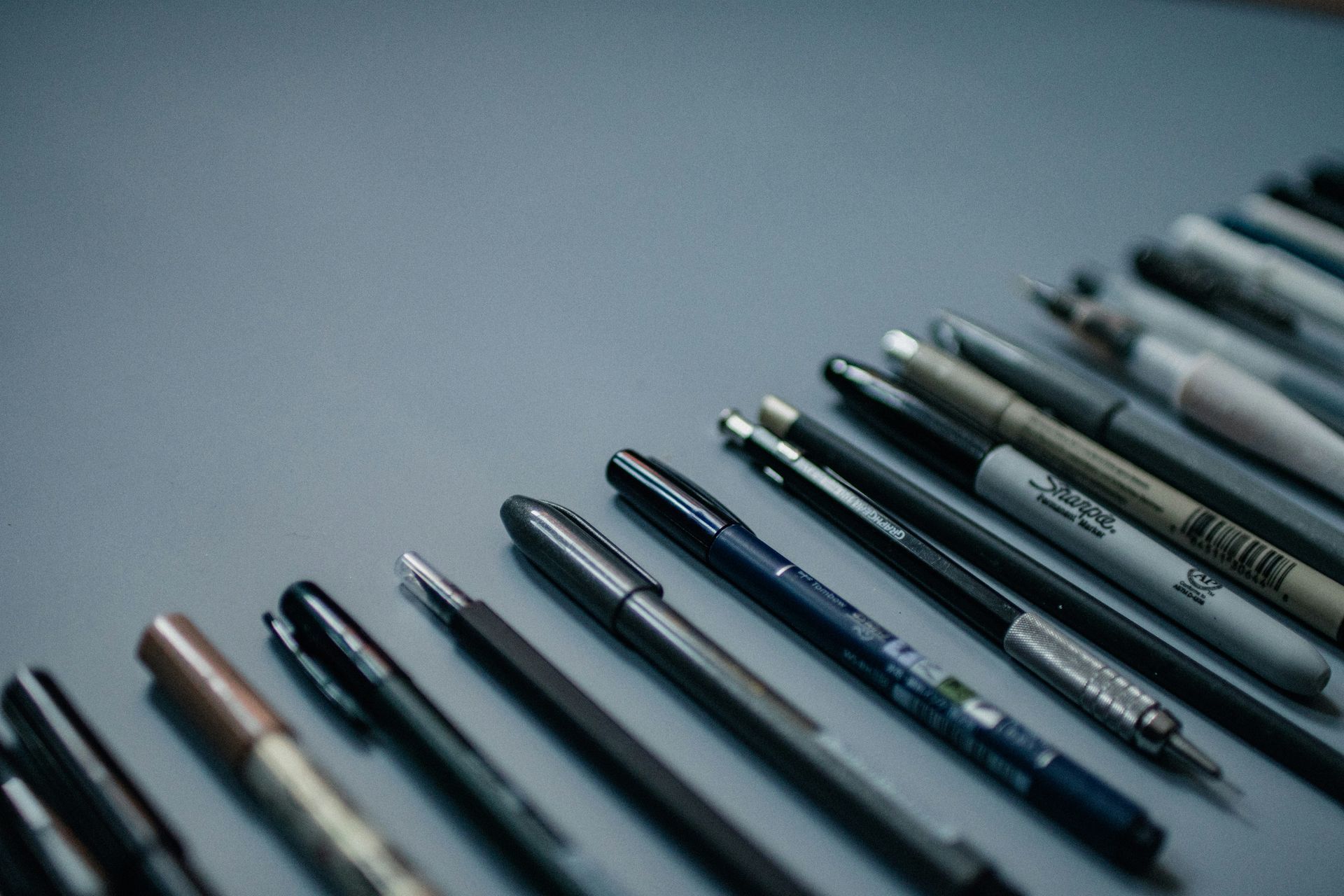 A bunch of pens and pencils are lined up on a table.