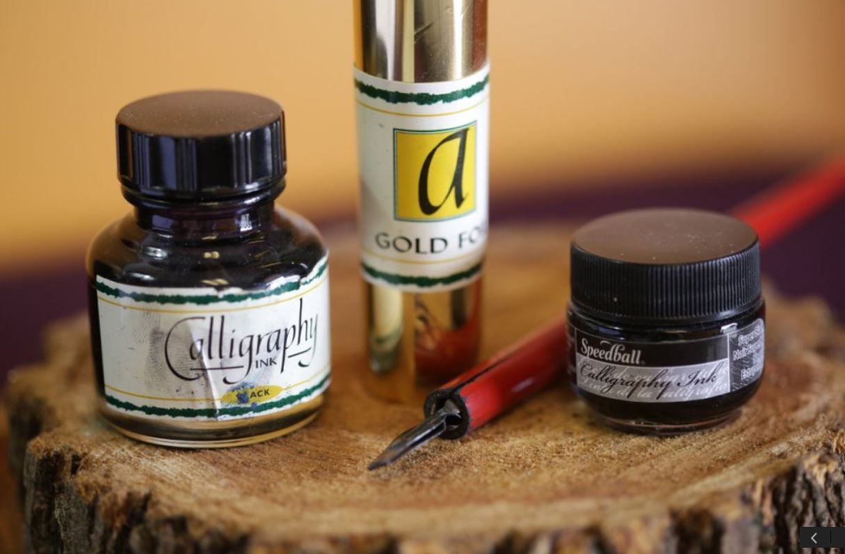 Three bottles of calligraphy ink and a pen on a piece of wood