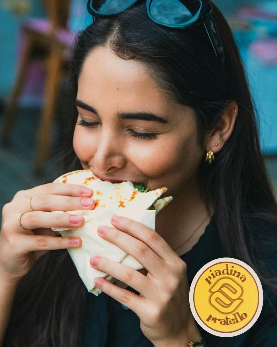 Una donna sorridente mangia una piadina avvolto in una busta 
