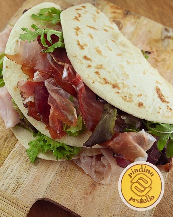 Apri il panino con focaccia, lattuga, prosciutto e salsa di pomodoro su un tagliere di legno.