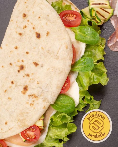Primo piano di un wrap con lattuga, pomodoro, cetriolo e formaggio su un piatto.