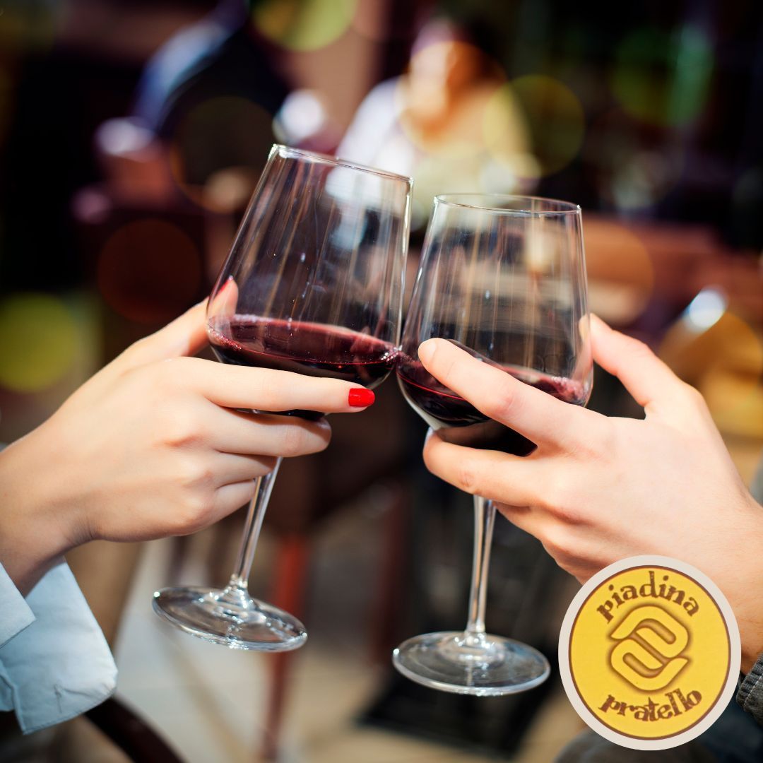 Mani che alzano calici di vino rosso in un brindisi a un tavolo di un ristorante illuminato da luci soffuse.