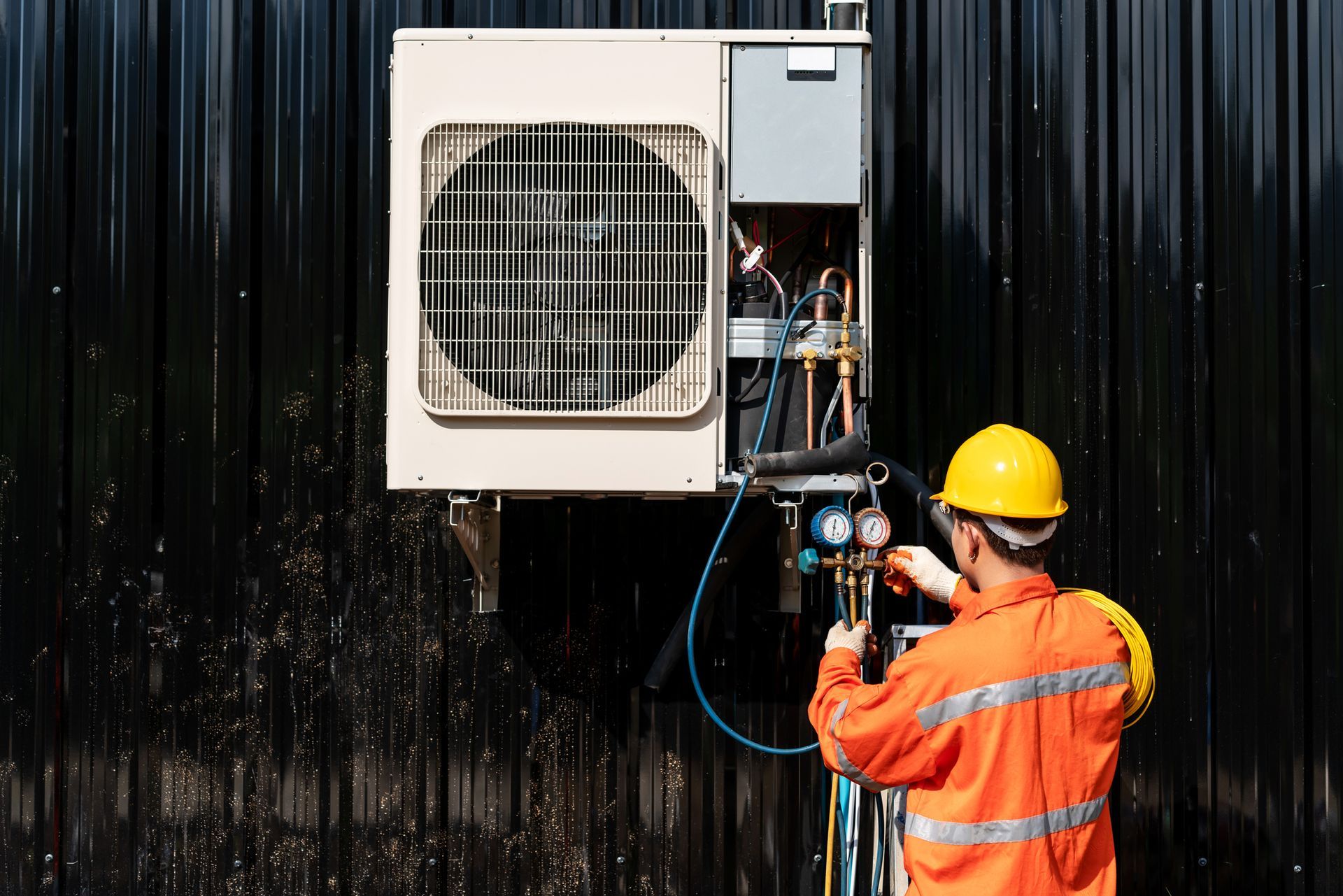 Male technician uses a pump to check and repair an exterior air conditioner.