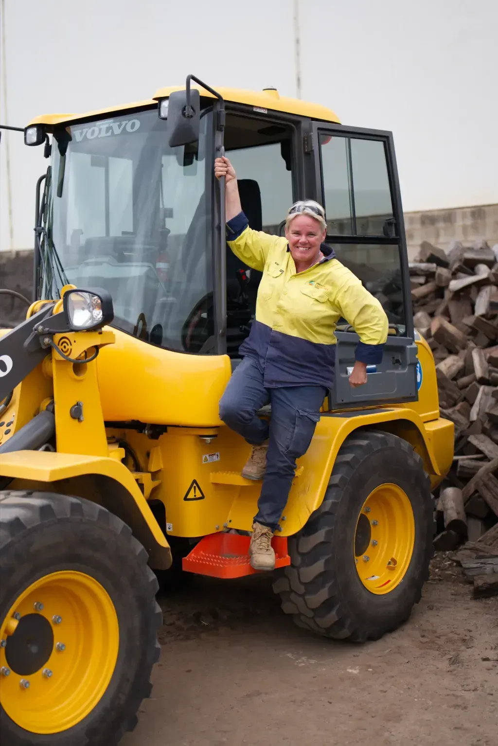 A woman is sitting on the side of a yellow mini digger.