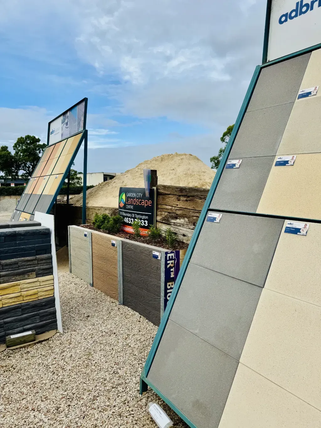 A display of paver tiles in a gravel area with a garden city landscape centre sign in the background.