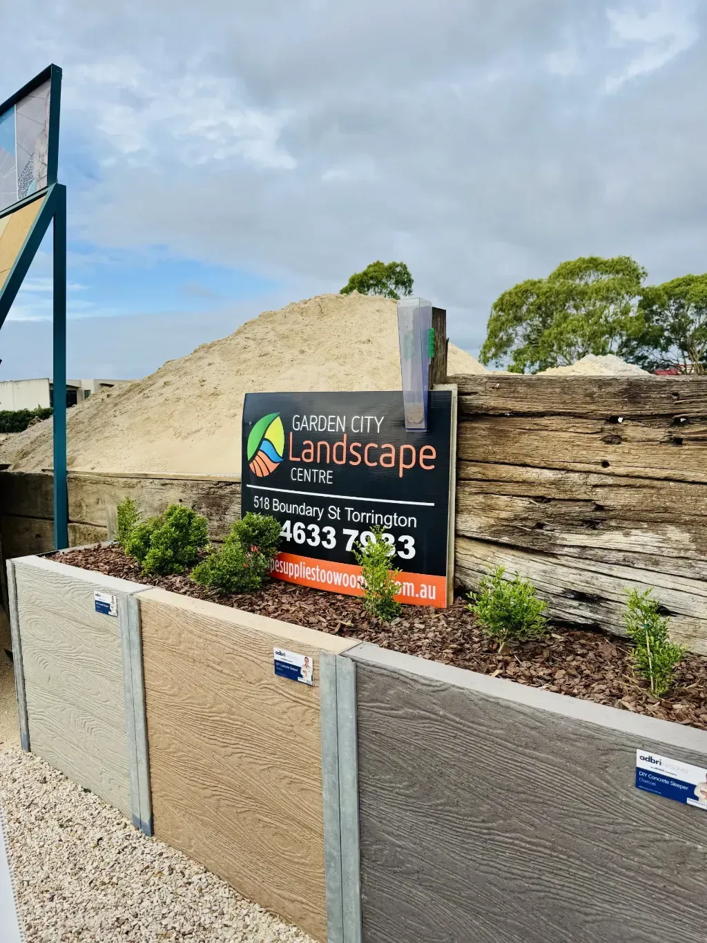 A sign for garden city landscape centre is sitting on top of a pile of mulch.