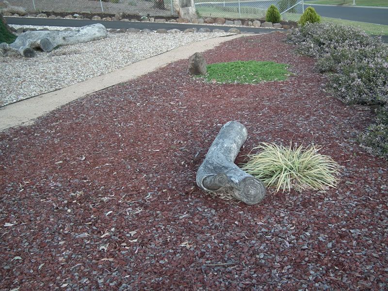 A wooden log sitting on red mulch in a garden
