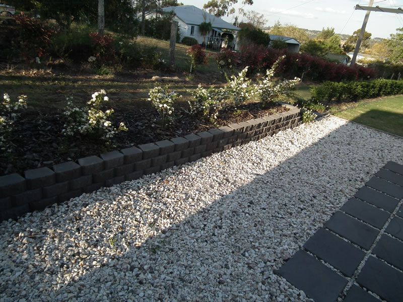 A gravel path with a brick wall and a house in the background