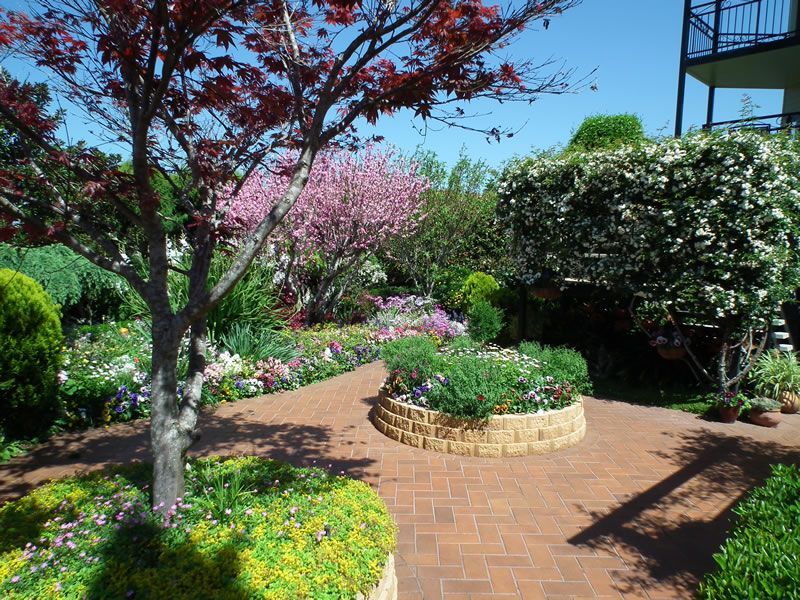 A garden with a brick walkway surrounded by flowers and trees