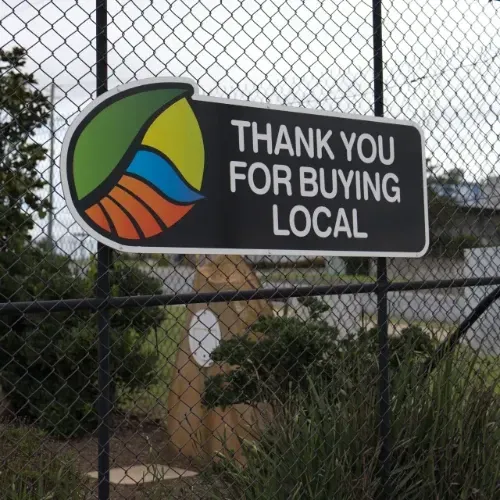 A sign on a chain link fence says thank you for buying local