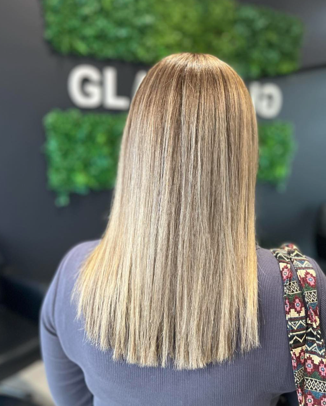A woman with long blonde hair is standing in a salon — Glam Hair and Beauty in Woy Woy, NSW