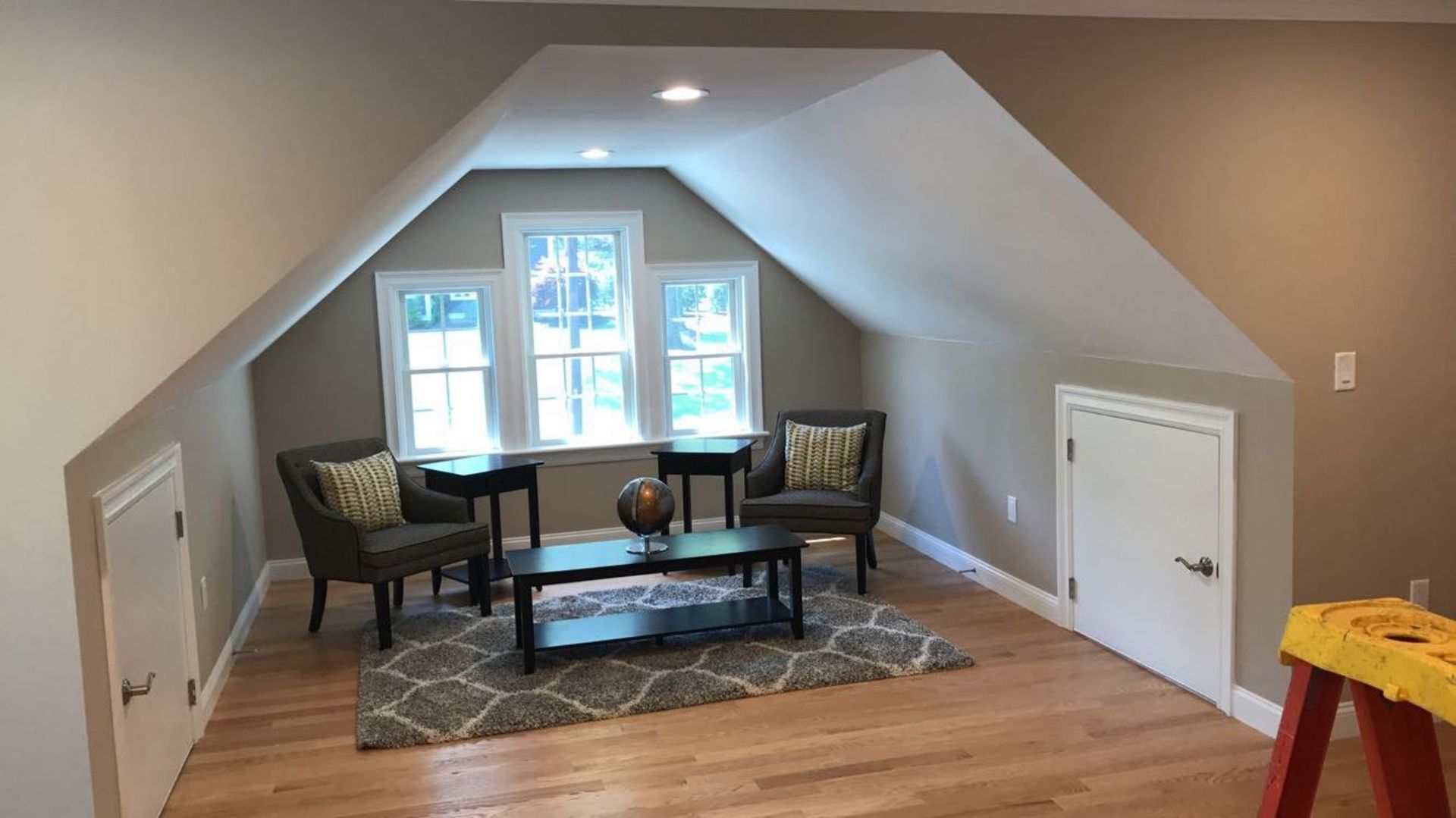 An attic with two chairs , a coffee table , and a window.
