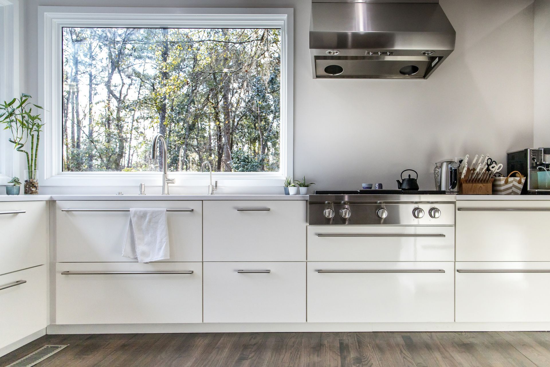 A kitchen with white cabinets and stainless steel appliances and a large window.