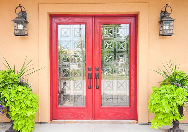 There are two potted plants in front of a red door.