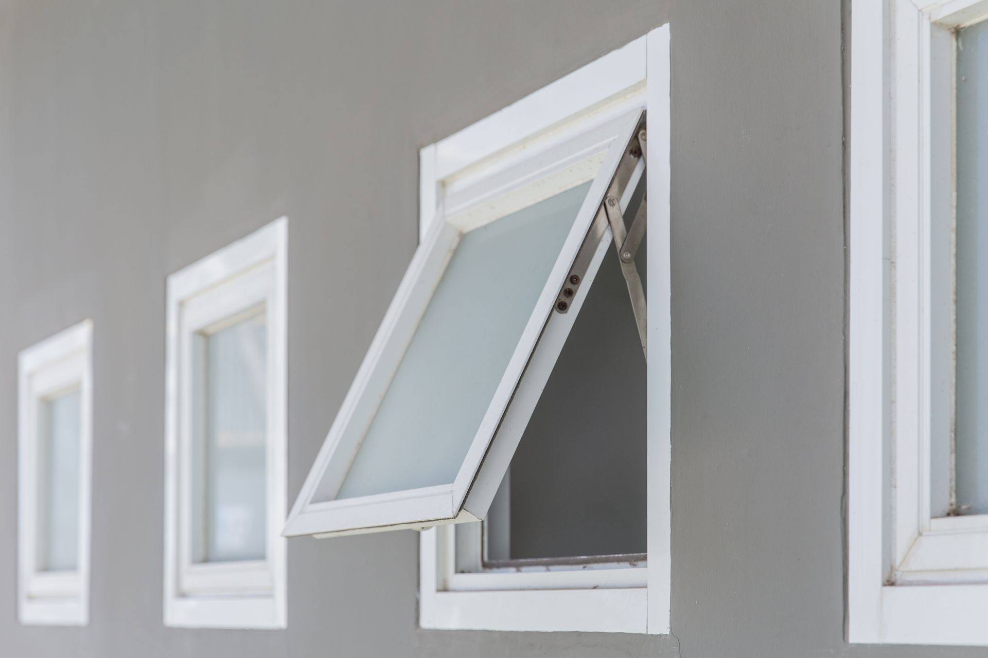 A row of white windows on a gray wall with one window open.