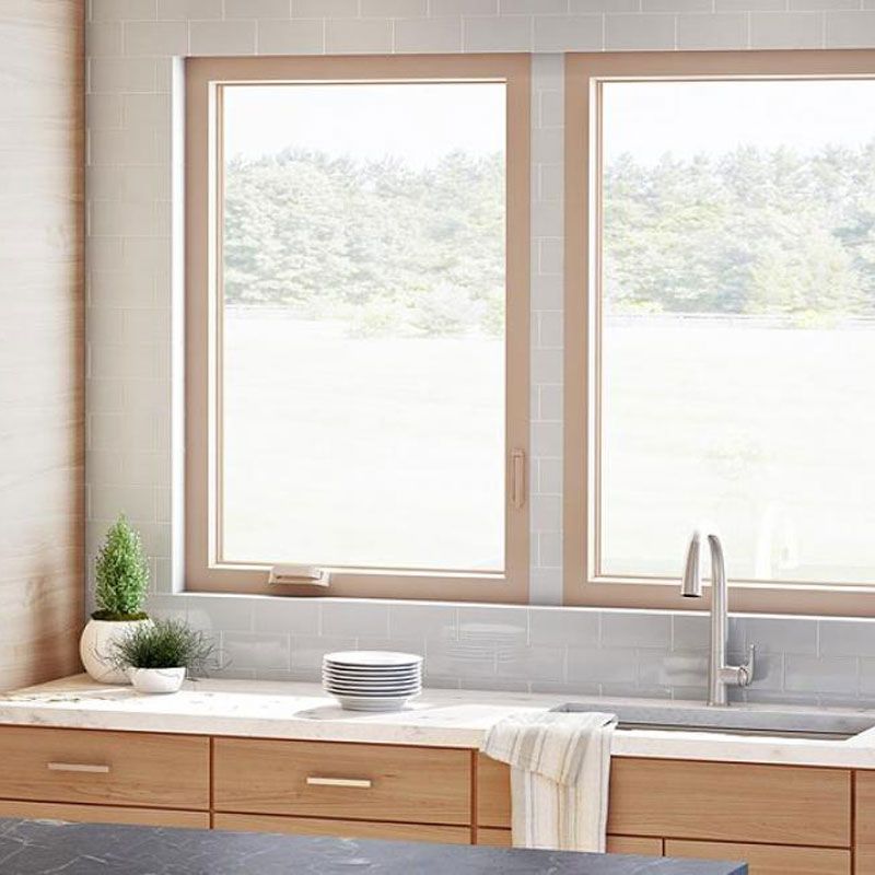 A kitchen with a sink , two windows , and wooden cabinets.