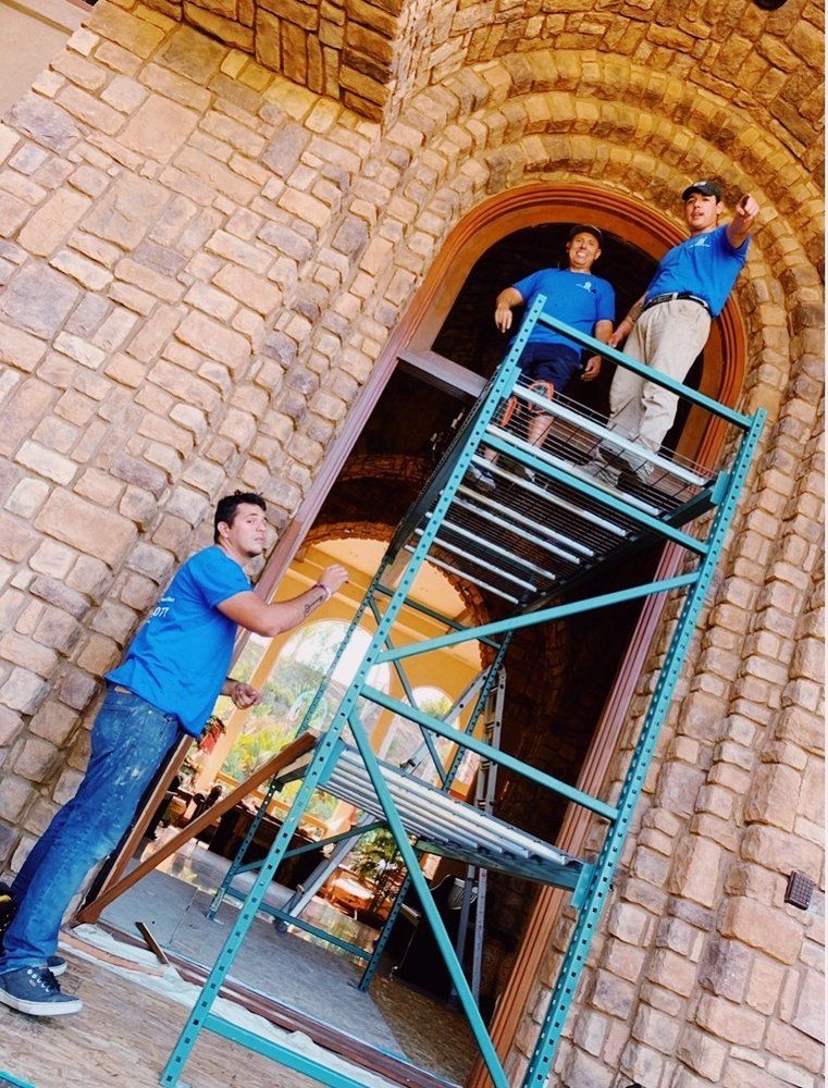 Three men are standing on a scaffolding in front of a brick building.