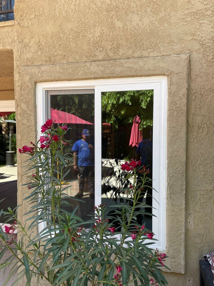 A man is standing in front of a window with a red umbrella reflected in it.